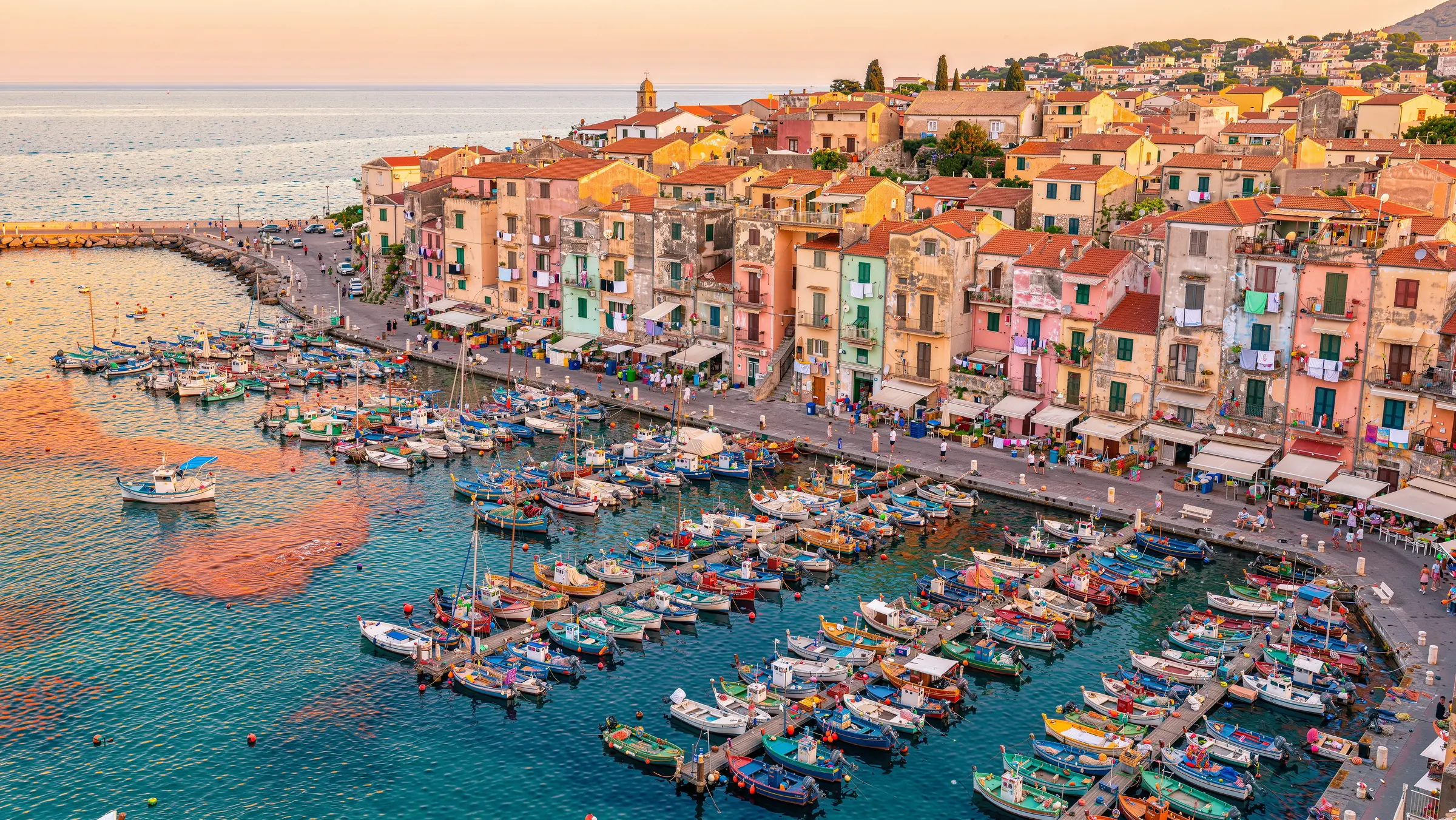 Aerial view of a Mediterranean harbor town at golden hour with hundreds of colorful boats and pastel houses
